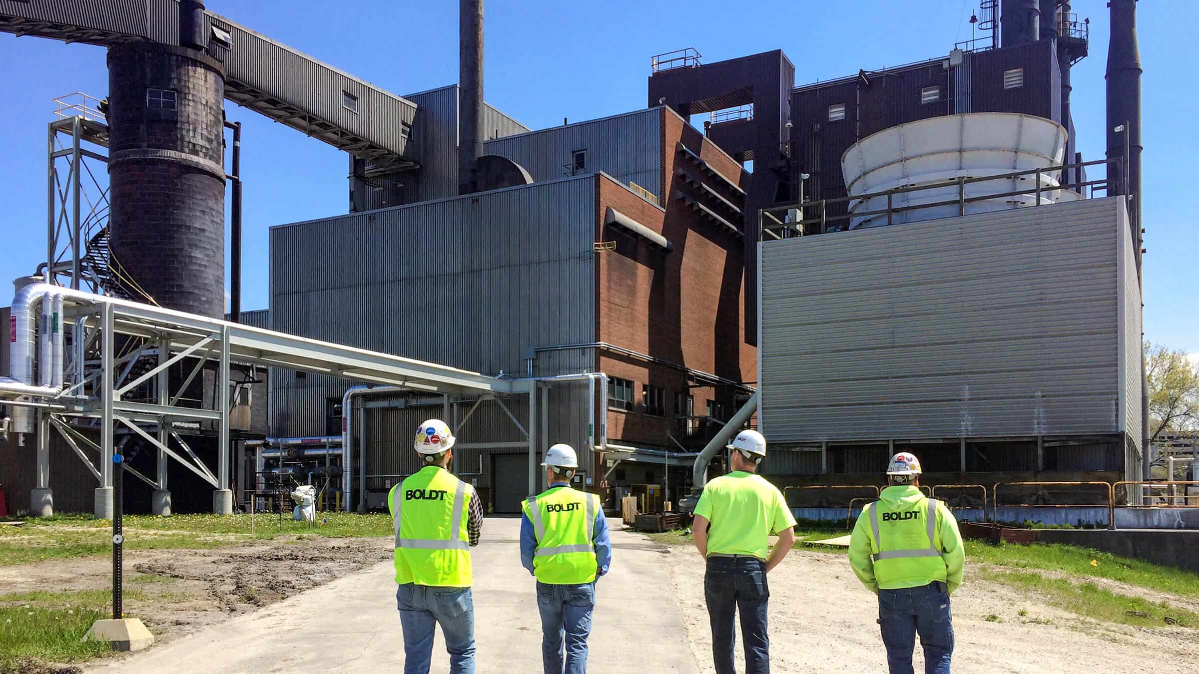 four boldt employees wearing neon vests facing towards power plant