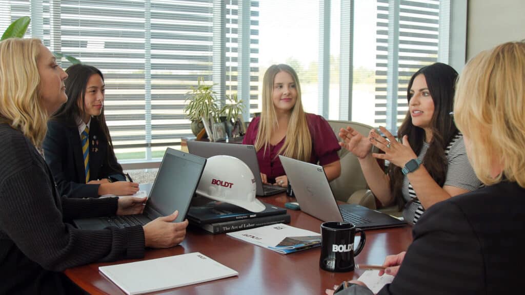 group of 5 women sitting around a desk in an office