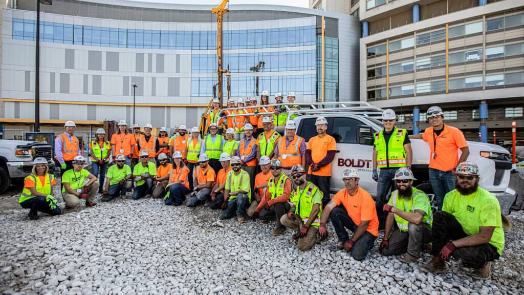 large group of construction workers pose for picture in front of construction site